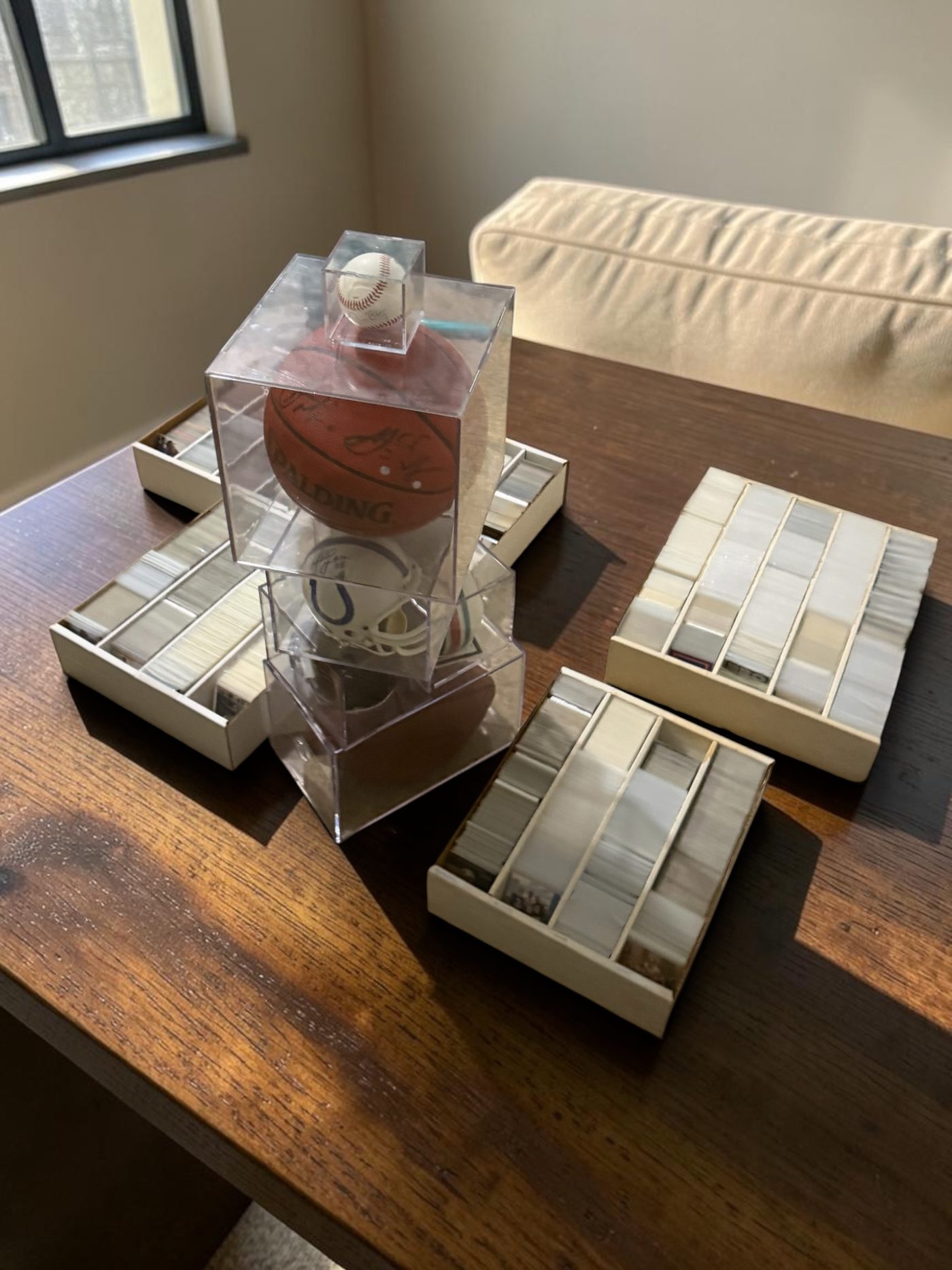 Four boxes of sleeved sports cards on a dining table alongside a signed baseball, a signed basketball and a signed Colts mini helmet, at a collection call in the Houston area