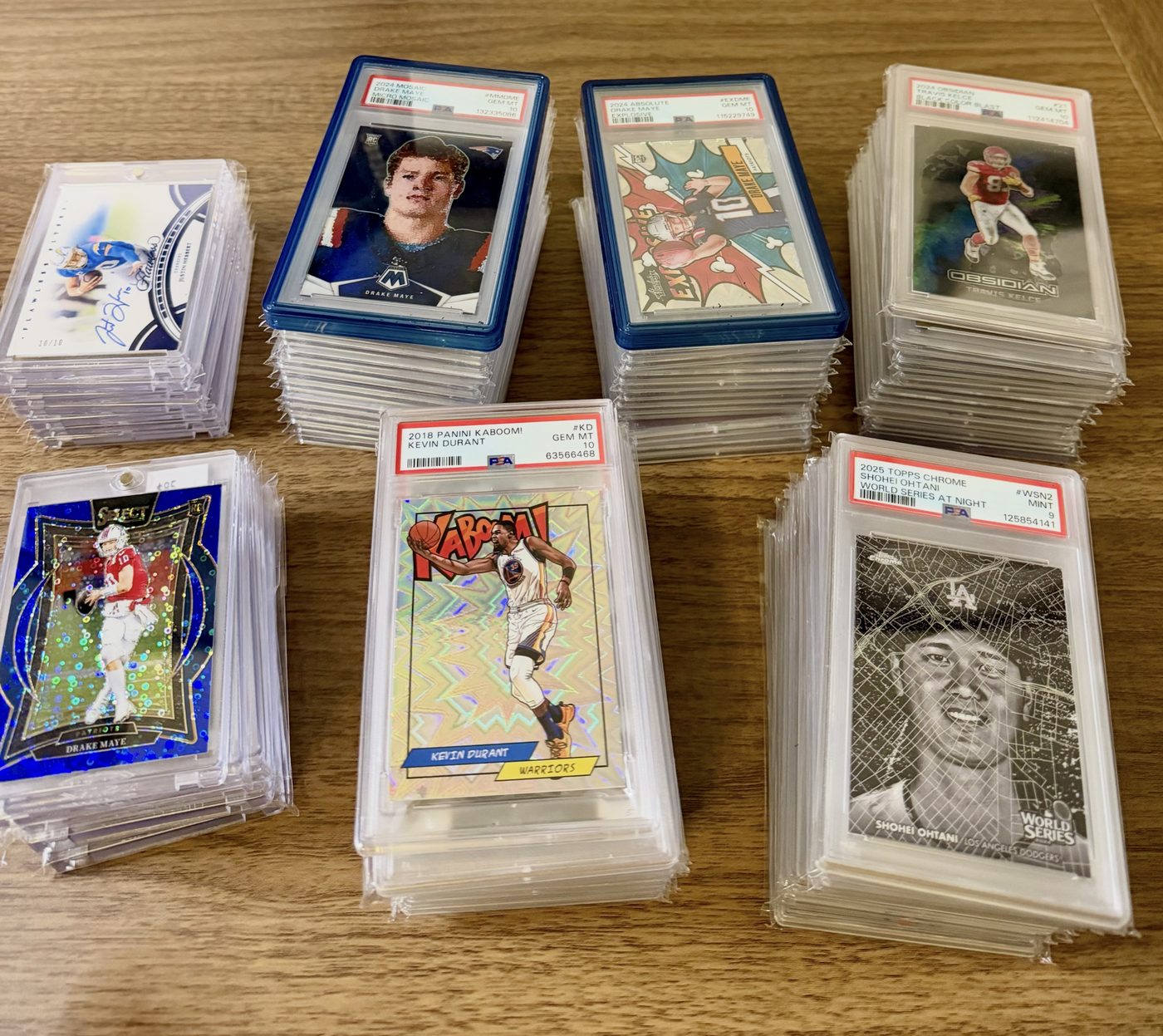 Stacks of graded cards including a PSA 10 2024 Mosaic Drake Maye, PSA 10 Travis Kelce Black Color Blast, PSA 10 2018 Kaboom Kevin Durant and a PSA 9 2025 Topps Chrome Shohei Ohtani World Series at Night, from the Conroe Card Show in January 2026