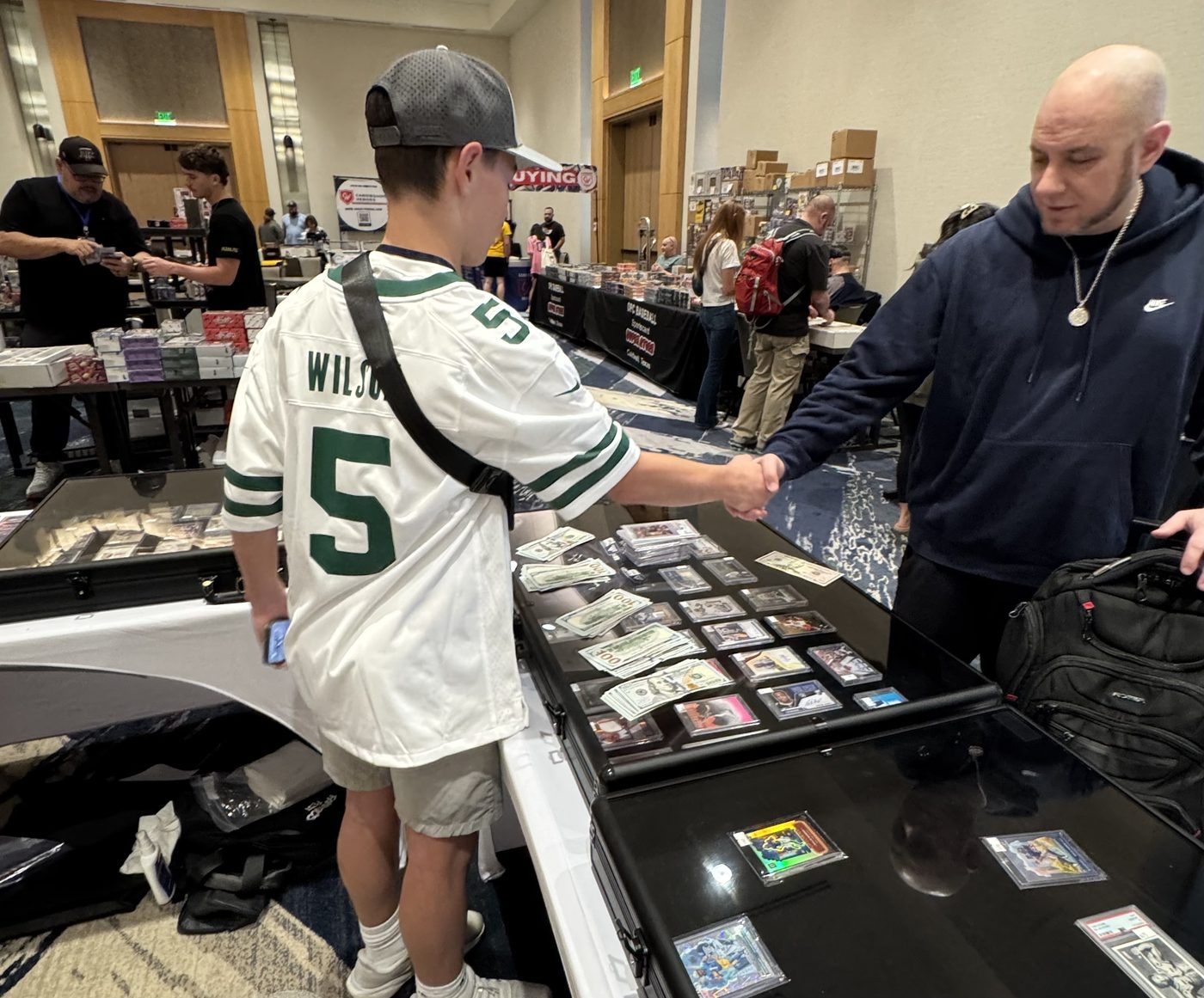 Grayson shaking hands on a deal across a case of graded cards and cash at the Conroe Card Show, November 2025