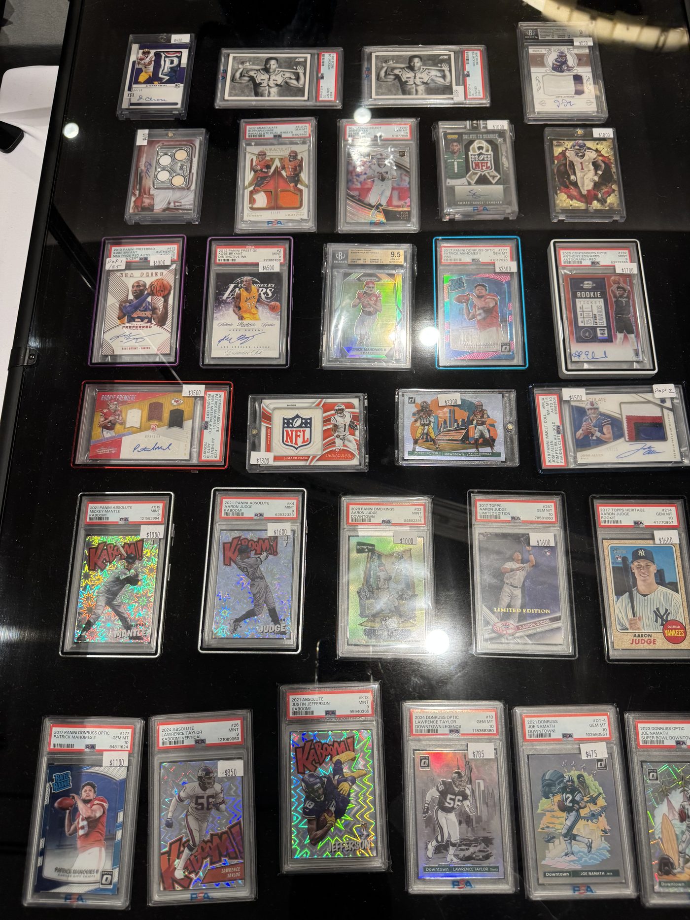 A display case of graded slabs at the Conroe Card Show, October 2025, including Kaboom inserts, Downtowns, Kobe Bryant autographs, Patrick Mahomes rookies and Aaron Judge cards