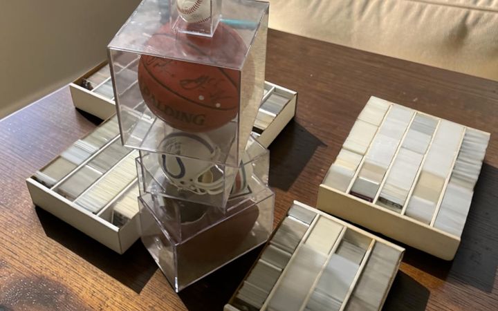 Four boxes of sleeved sports cards on a dining table alongside a signed baseball, a signed basketball and a signed Colts mini helmet, at a collection call in the Houston area