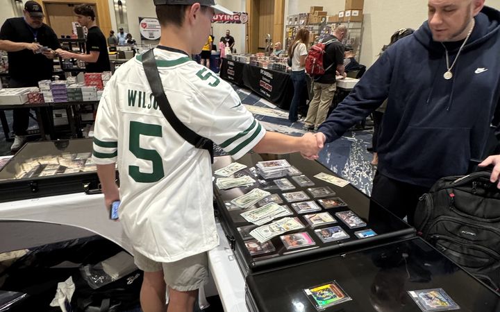 Grayson shaking hands on a deal across a case of graded cards and cash at the Conroe Card Show, November 2025