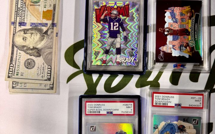 Four graded cards and cash on the Slabs & Signatures table at the Space City Card Show: a Tom Brady Kaboom PSA 9, a LeBron James Downtown variation PSA 10, and two Brady Downtowns